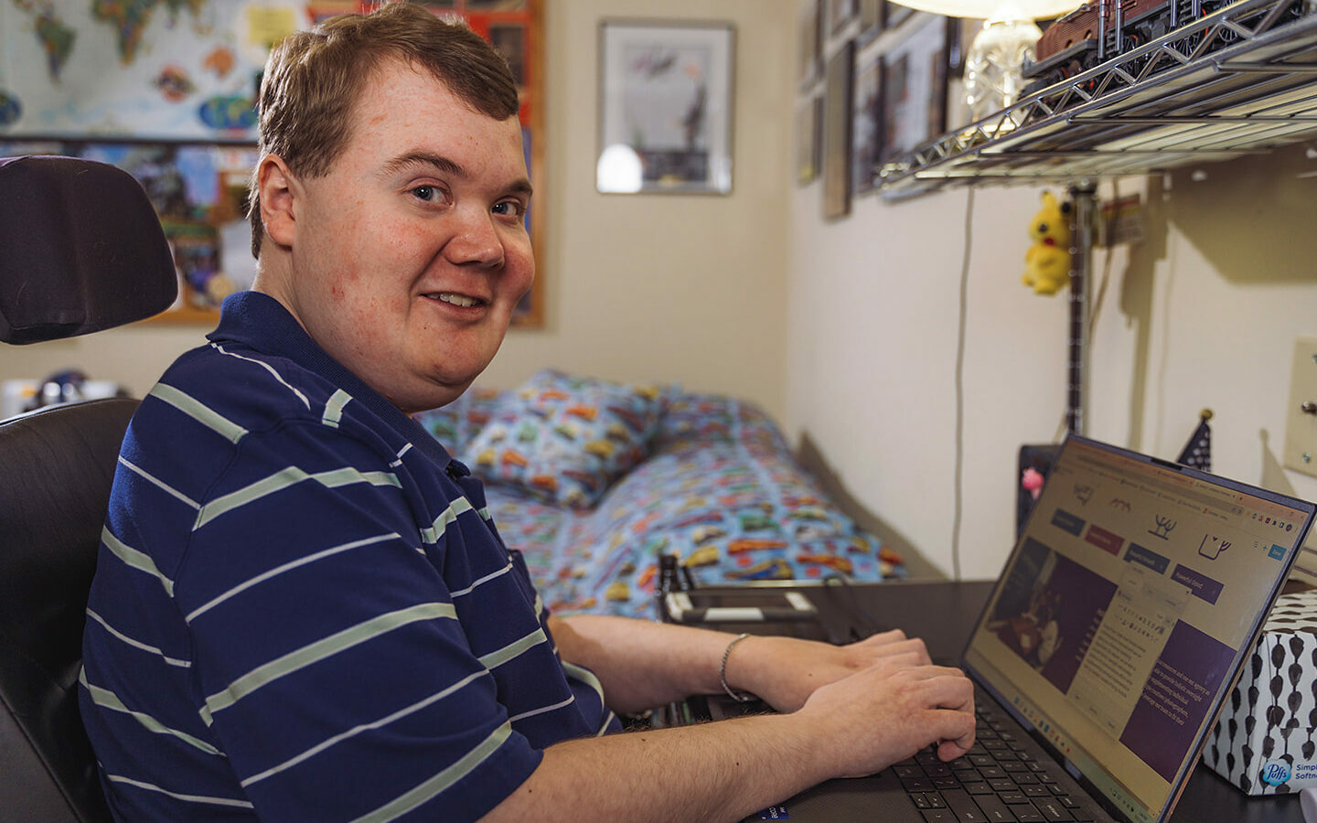 A man with Duchenne muscular dystrophy wearing a striped short-sleeved dress shirt types on a laptop computer.